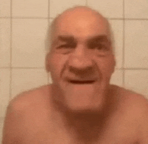 an elderly man without a shirt is smiling in a bathroom .