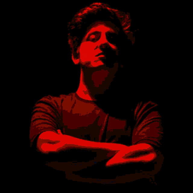 a man in a red shirt with his arms crossed in the dark