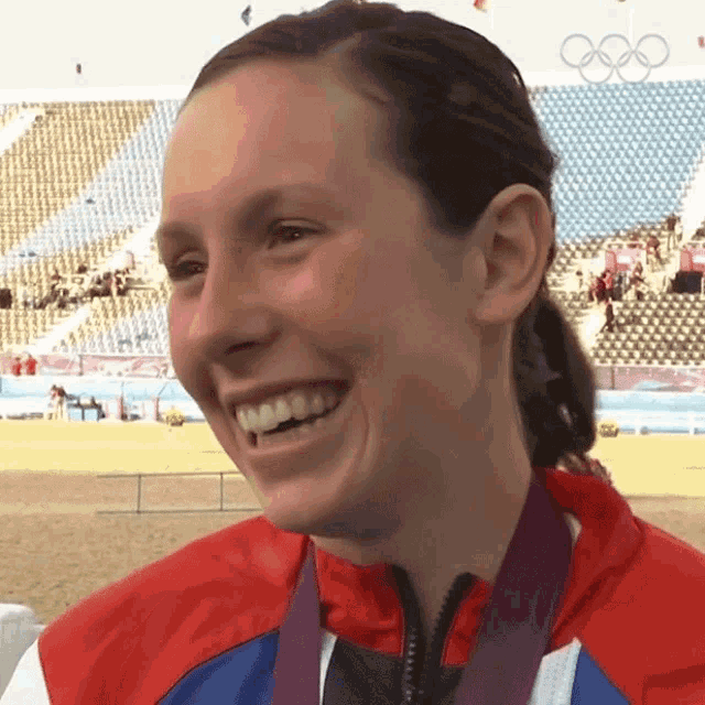 a woman with a medal around her neck is smiling in front of empty stadium seats