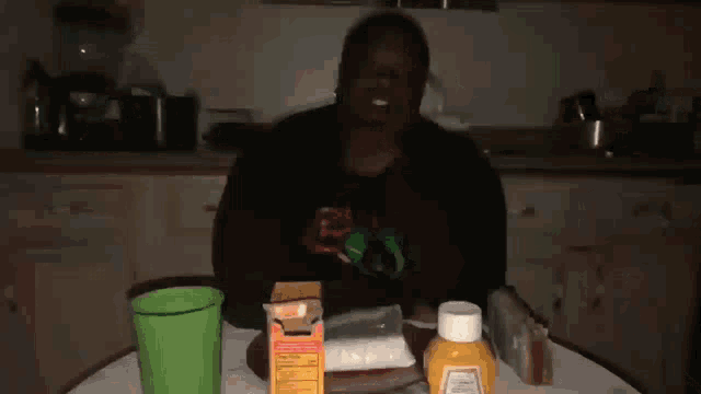 a person sitting at a table with a bottle of mustard and a box of pills