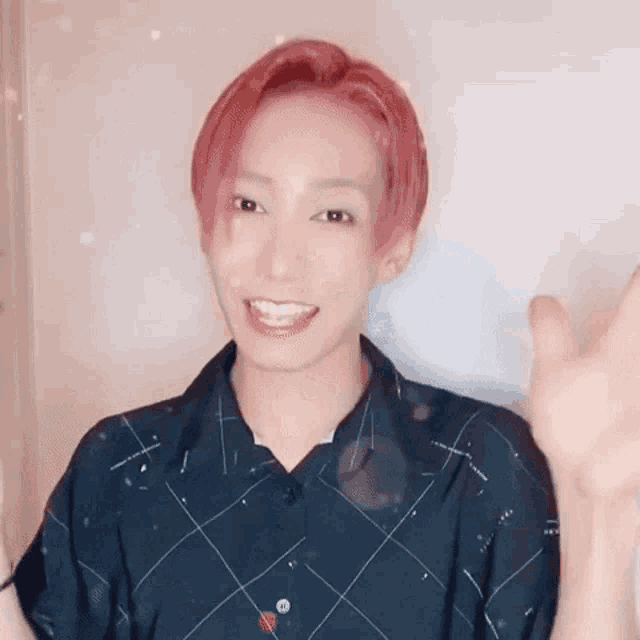 a young man with red hair is smiling and waving at the camera while wearing a plaid shirt .