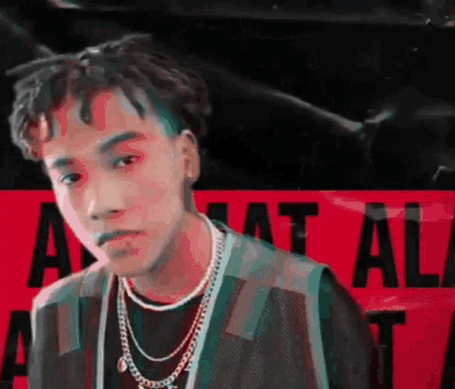 a young man with dreadlocks is wearing a necklace and a black shirt .