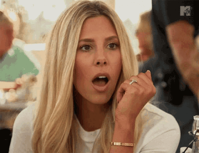 a woman with a ring on her finger is sitting at a table with her mouth open