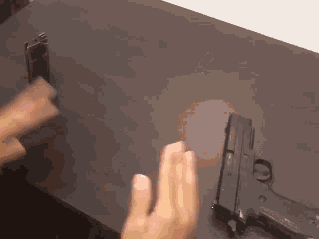 a person is putting a magazine into a gun on a wooden table