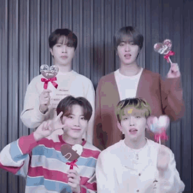 a group of young men are holding heart shaped lollipops and making peace signs .