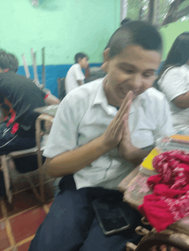 a boy sits at a desk with his hands folded in front of his face