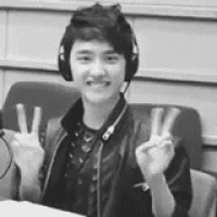 a young man wearing headphones and a leather jacket is sitting in a chair giving a peace sign .
