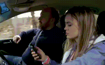a man and a woman are sitting in a car and the woman is looking at her cell phone