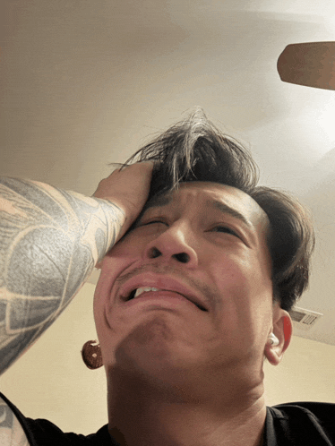 a man with a tattoo on his arm holds his hand to his head
