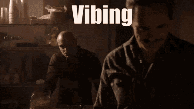 a man with a mustache stands in front of a sign that says " vibing "
