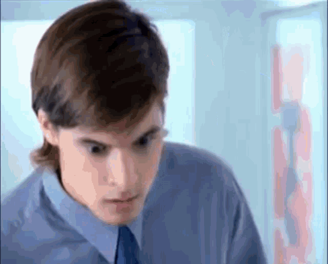 a man in a blue shirt and blue tie is looking at the camera .