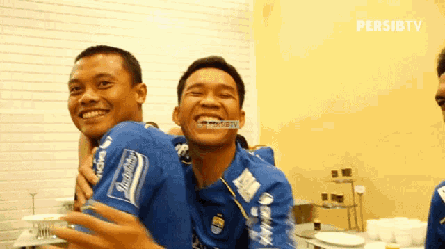 two men are hugging each other and one of their shirts says indosat