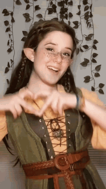 a woman in a green and yellow dress making a heart shape with her hands