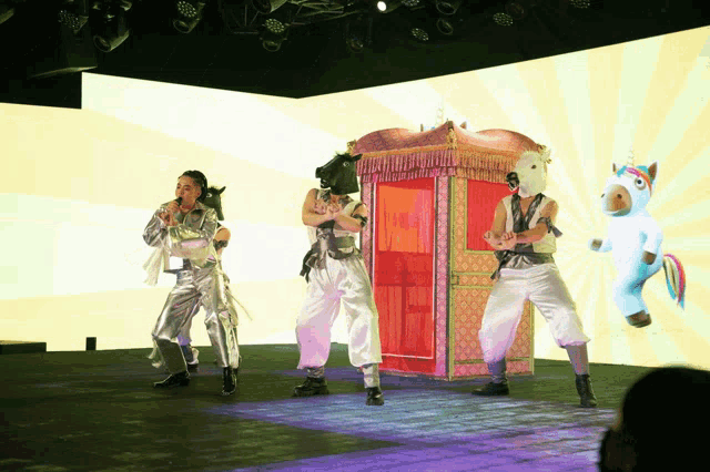 a group of people wearing horse masks are dancing on a stage with a unicorn in the background