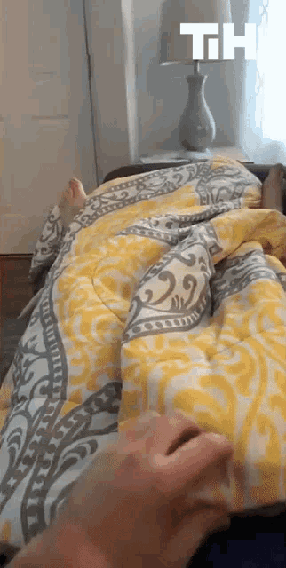 a person is laying on a bed with a yellow and grey comforter and a lamp with the letters th on it