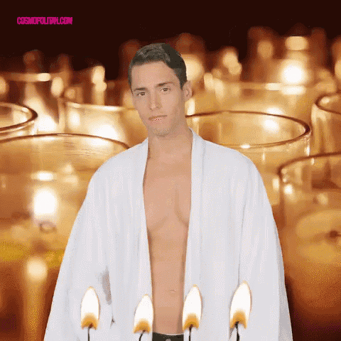 a shirtless man in a white robe stands in front of lit candles with cosmopolitan.com written on the bottom right