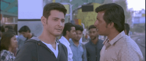 two men are standing next to each other and talking in a crowded street .