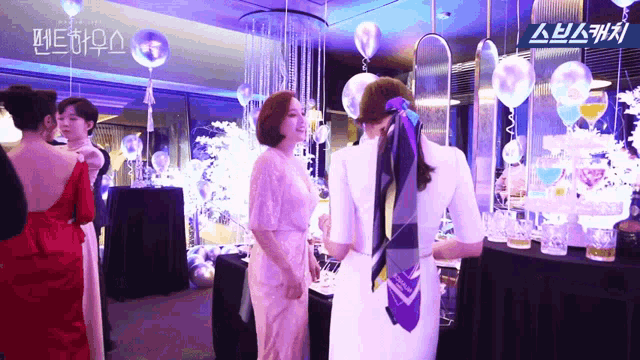 a group of women are standing in a room with balloons and flowers
