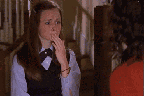 a woman in a school uniform is biting her nails while talking to another woman in a red shirt .