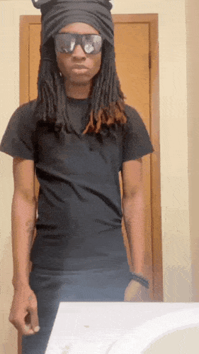 a man with dreadlocks wearing sunglasses and a black shirt stands in front of a mirror