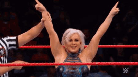 a woman is standing in a wrestling ring with her arms in the air and a referee behind her .