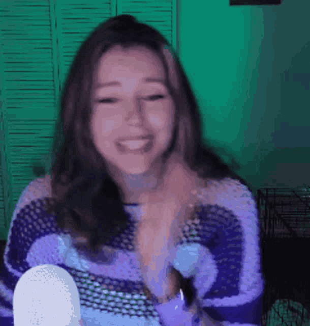 a woman in a purple and blue striped sweater is smiling and holding a microphone .