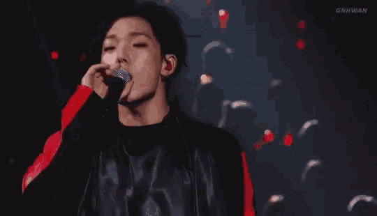 a young man is singing into a microphone on a stage in a dark room .