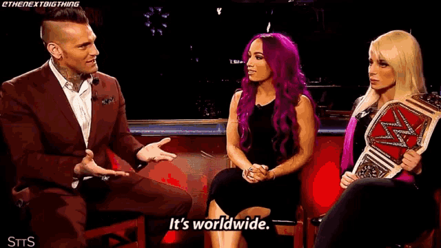 a man and two women are sitting next to each other on a couch and talking .