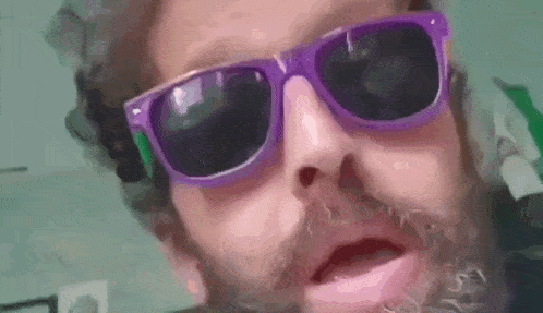 a man with a beard wearing purple sunglasses and making a funny face .