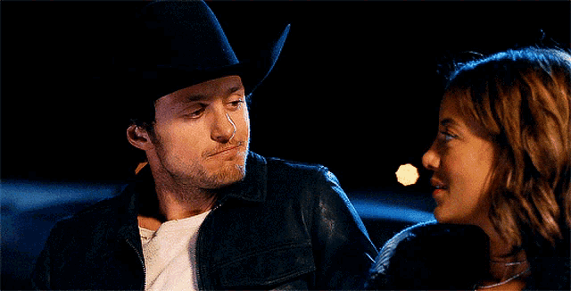 a man in a cowboy hat is looking at a woman in a leather jacket