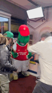 a group of people are standing around a mascot wearing a shirt that says arsenal fc