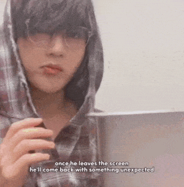 a young man wearing glasses and a plaid shirt is standing in front of a computer screen .