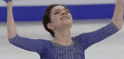 a woman in a blue dress is skating on a rink with her arms in the air .
