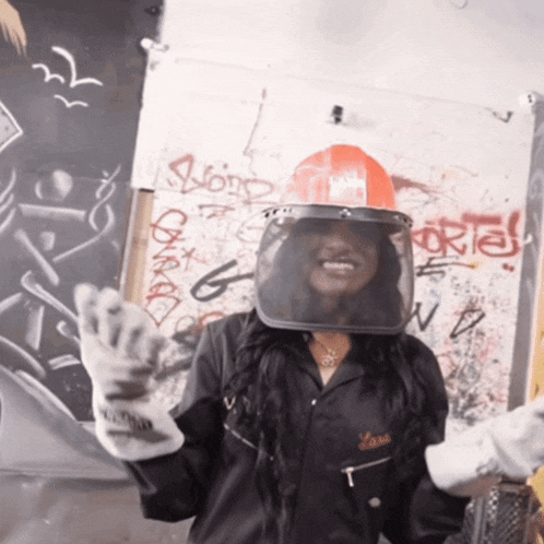 a woman wearing a hard hat and gloves stands in front of a graffiti wall