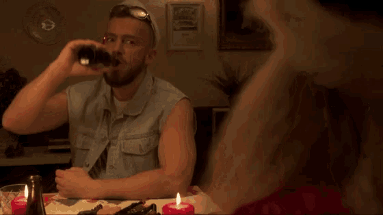 a man in a denim vest drinks from a bottle while sitting at a table