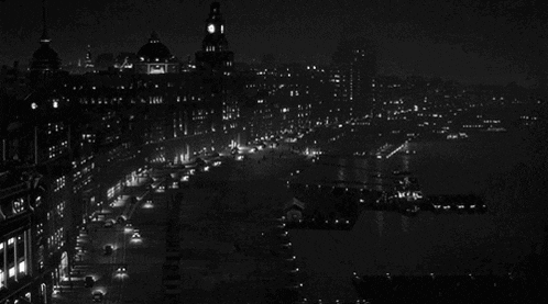 a black and white photo of a city at night with a clock tower in the middle