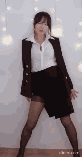 a woman in a white shirt and black skirt is dancing in front of a white wall .