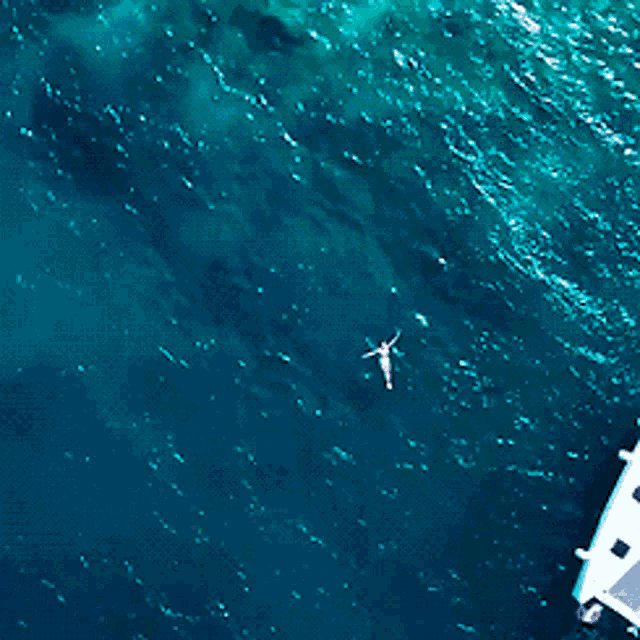 an aerial view of a person swimming in the ocean near a boat