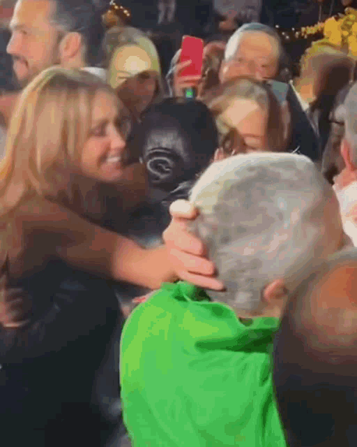 a woman in a green shirt is hugging a man in a crowd of people