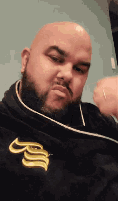 a bald man with a beard is wearing a black robe with the letter b on the front
