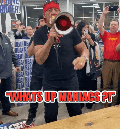 a man holding a megaphone in front of a crowd with the caption " whats up maniacs ? "
