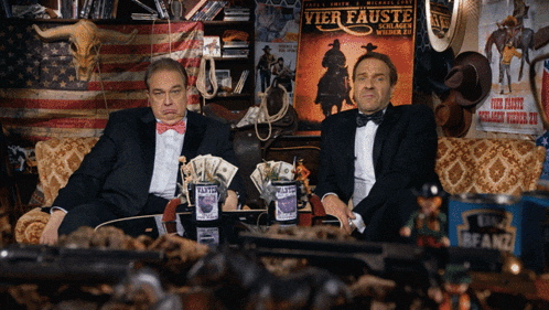two men sit on a couch in front of a poster for vier fauste