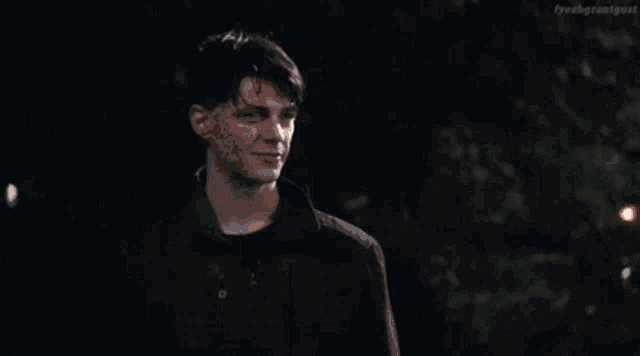 a young man in a black jacket is smiling at the camera in the dark .