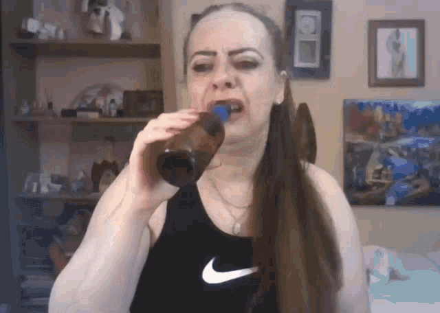 a woman in a nike tank top is drinking from a glass bottle .