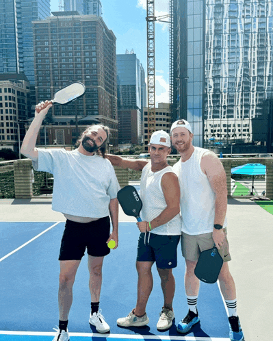three men standing on a tennis court with one holding a paddle that says " crew "