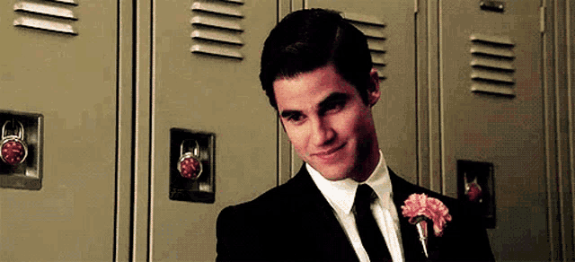 a man in a suit and tie is standing in front of a row of lockers .
