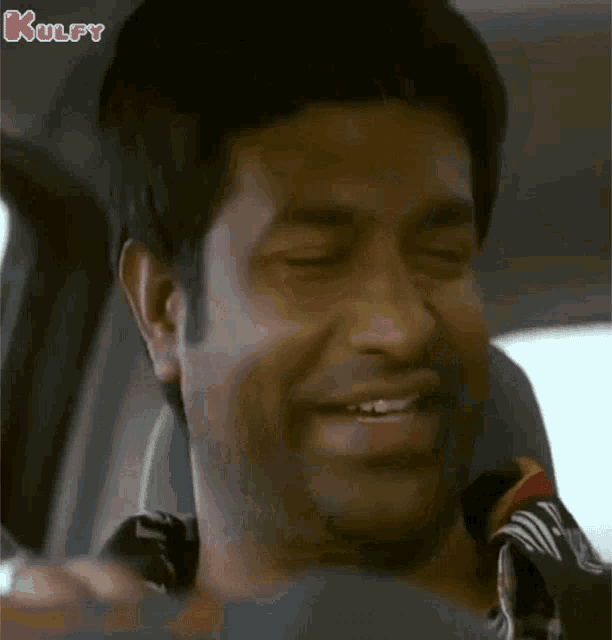 a man is smiling while sitting in a car with the word kulfy on the bottom right