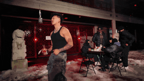 a man in a black tank top stands in front of a group of people sitting at tables