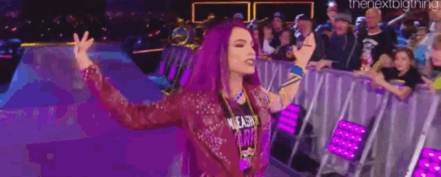 a woman with purple hair is standing in front of a crowd at a wrestling event .