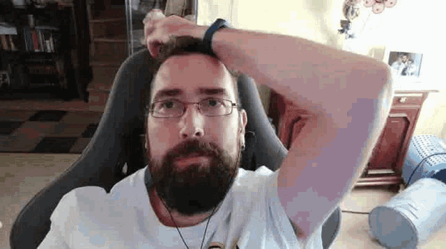 a man with a beard and glasses is sitting in a chair holding his head .